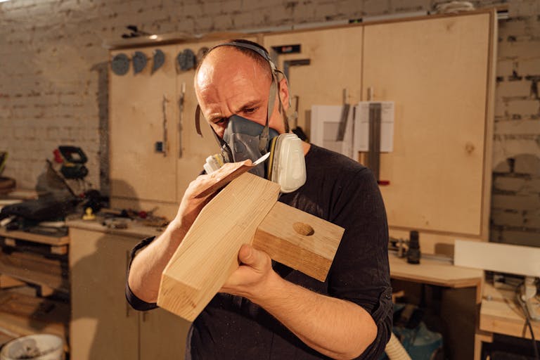 A focused carpenter uses hand tools to refine a wooden piece in an industrial workshop.