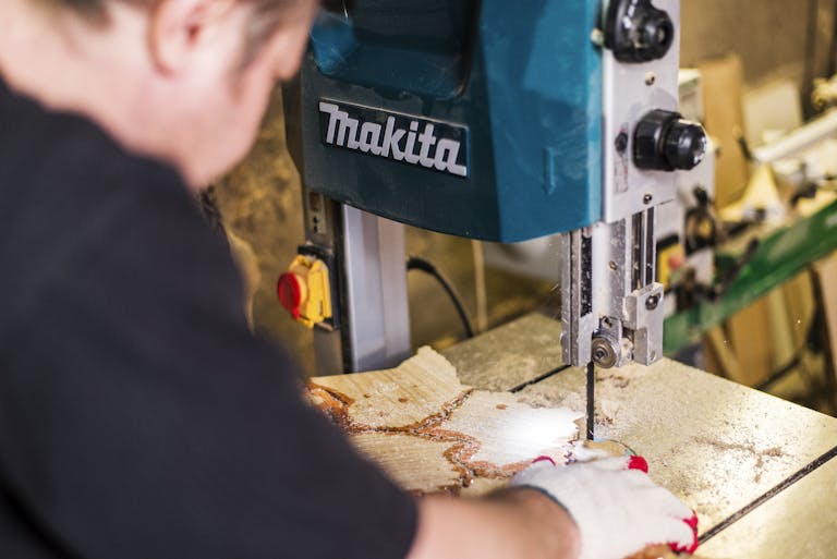Close-up of a worker using a Makita band saw in a woodworking shop highlighting precision.