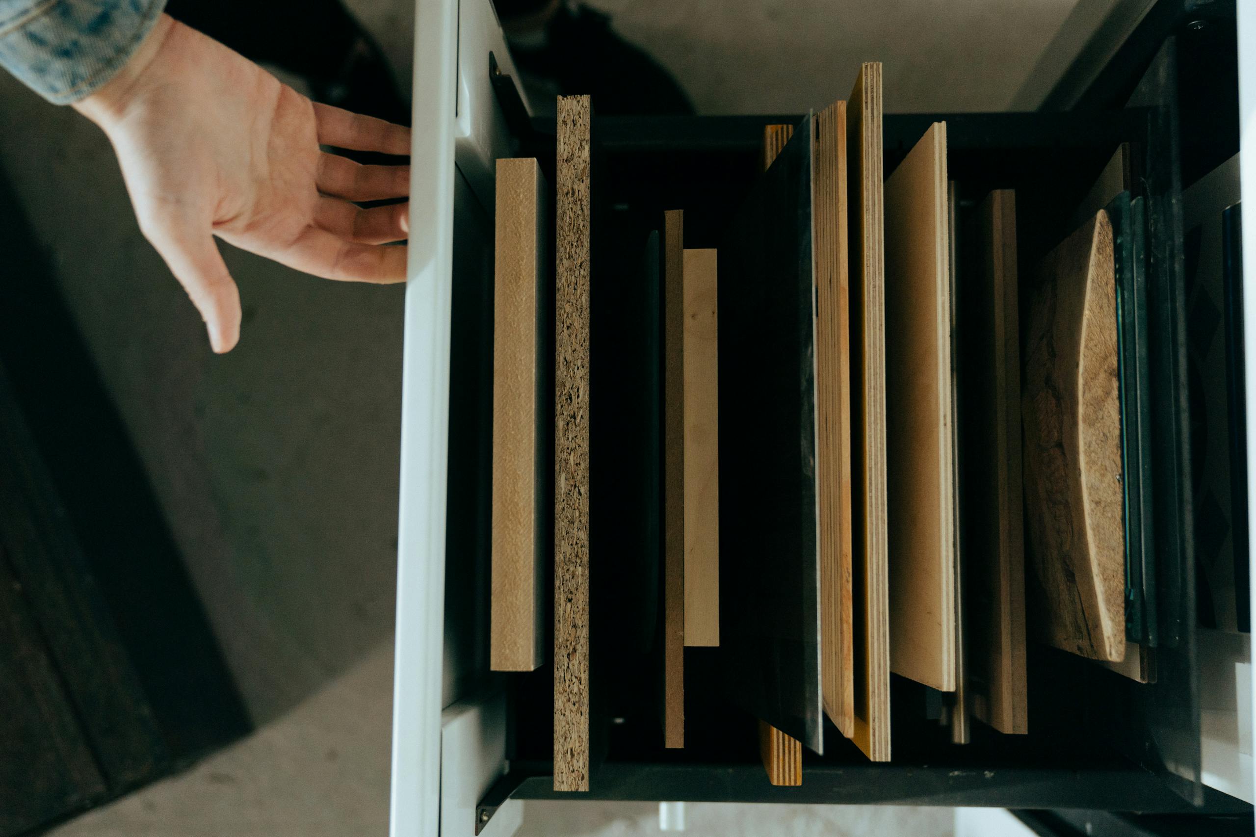 Top view of assorted wooden panels neatly arranged in a drawer with a hand reaching out.