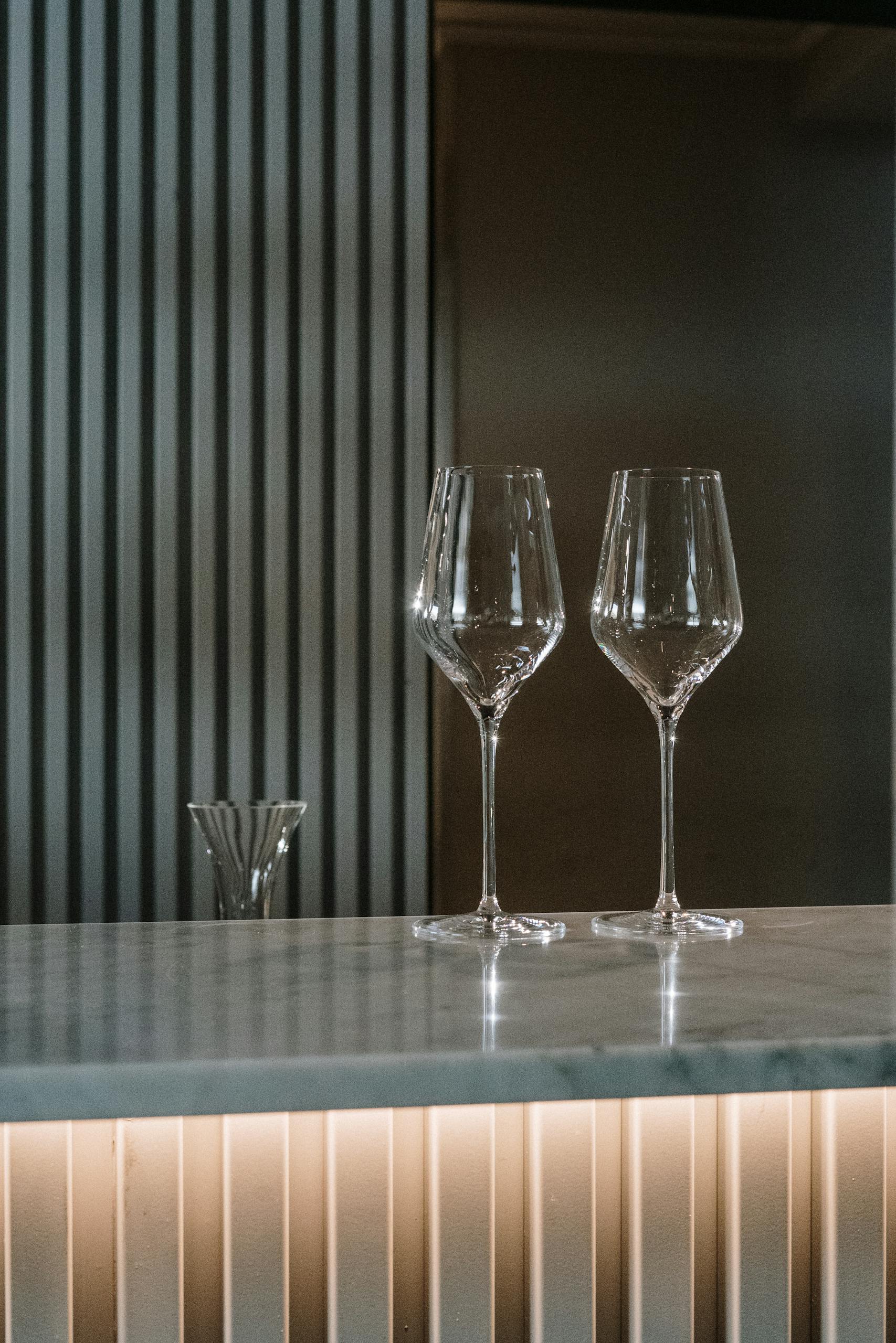 Two empty wine glasses on a sleek marble bar countertop in a modern interior setting.