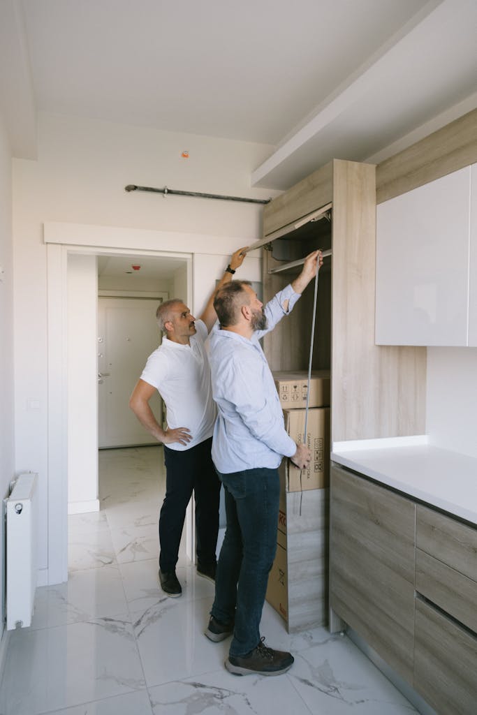 Two men measuring a modern kitchen cabinet for a renovation project in an apartment.